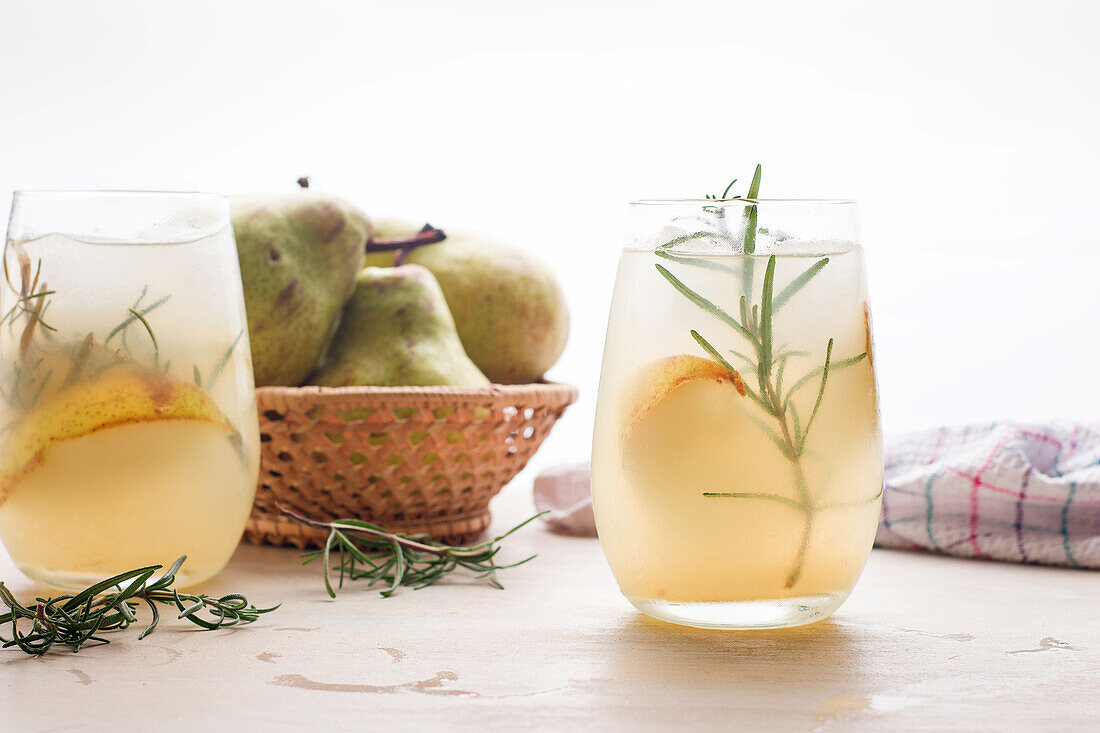 Cold pear cocktail in glasses with rosemary and ice cubes placed on table with fresh fruits