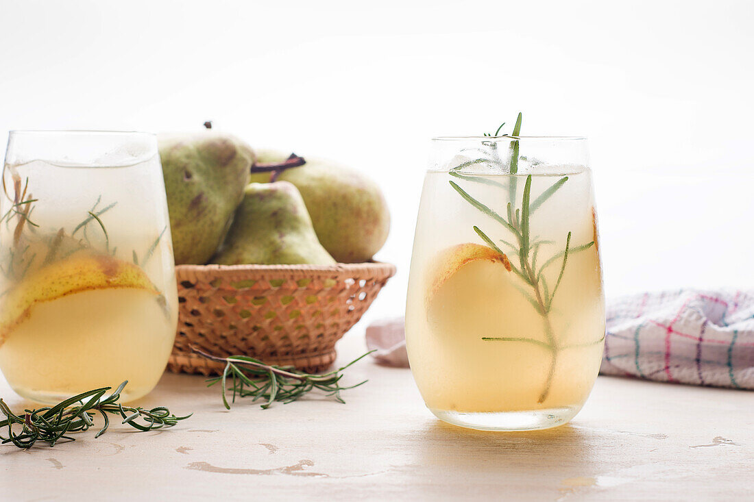 Kalter Birnencocktail in Gläsern mit Rosmarin und Eiswürfeln auf einem Tisch mit frischen Früchten