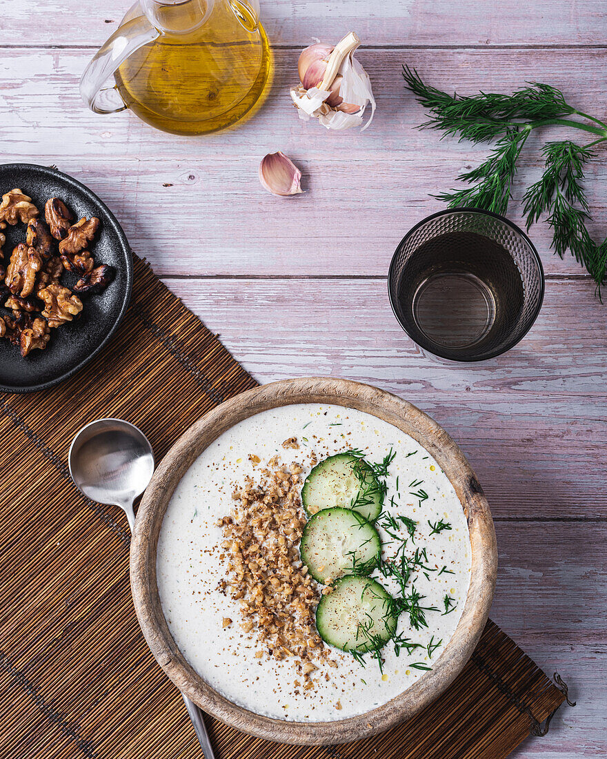 Schüssel mit traditioneller bulgarischer kalter Sommersuppe Tarator mit Joghurt neben einem Glas Wasser und einem Teller mit Nüssen von oben