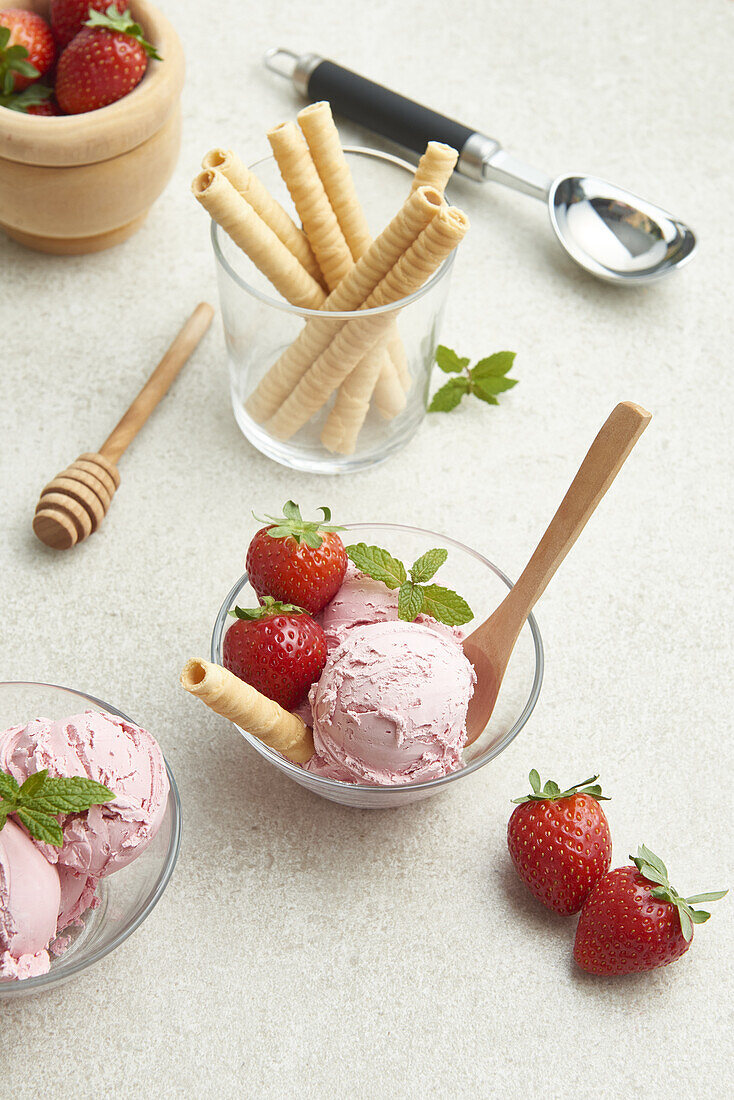 Hoher Blickwinkel auf köstliches hausgemachtes Erdbeereis in einer Glasschale mit Beeren und Waffelrolle in der Küche bei Tageslicht