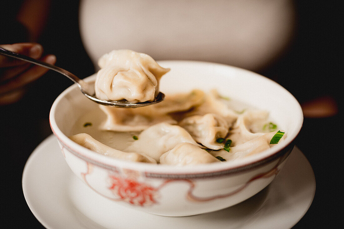 Nahaufnahme einer köstlichen Suppe mit Knödeln und Frühlingszwiebeln vor schwarzem Hintergrund