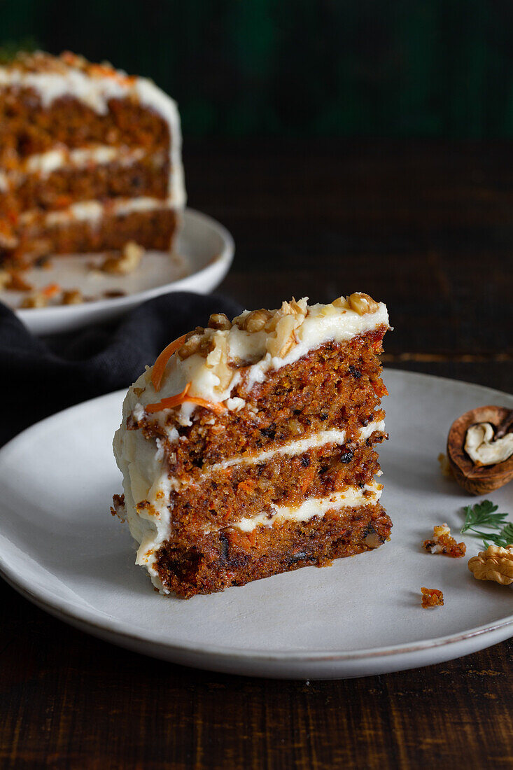 Yummy cake with cream cheese served on plates with fresh carrot slices and walnuts
