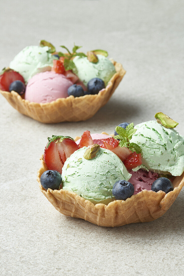 Blick von oben auf köstliches hausgemachtes Pistazien- und Erdbeereis in einer Waffelschale, dekoriert mit frischen Beeren, bei Tageslicht