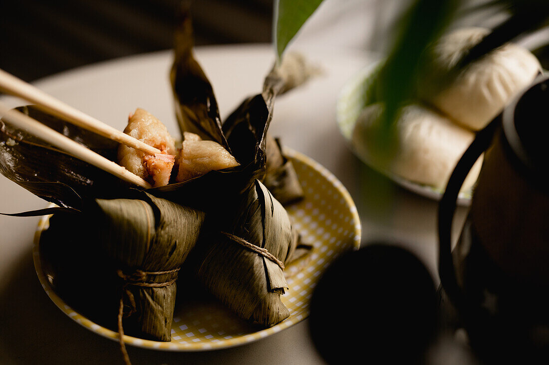Geöffnete und bedeckte Bambusblatt-Reisknödel auf einem hübschen karierten Teller mit Stäbchen obenauf
