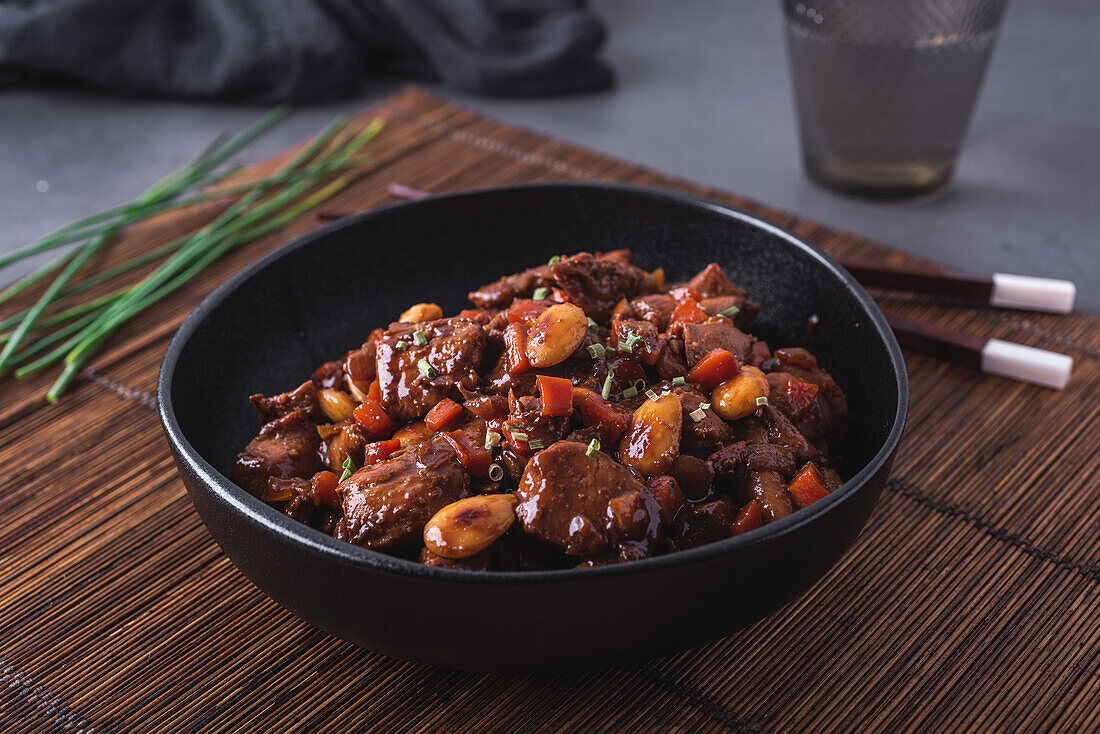 Schale mit asiatischem Hähnchenfleisch mit Mandeln und Gemüse in der Nähe von Bambus-Essstäbchen und Schnittlauch von oben