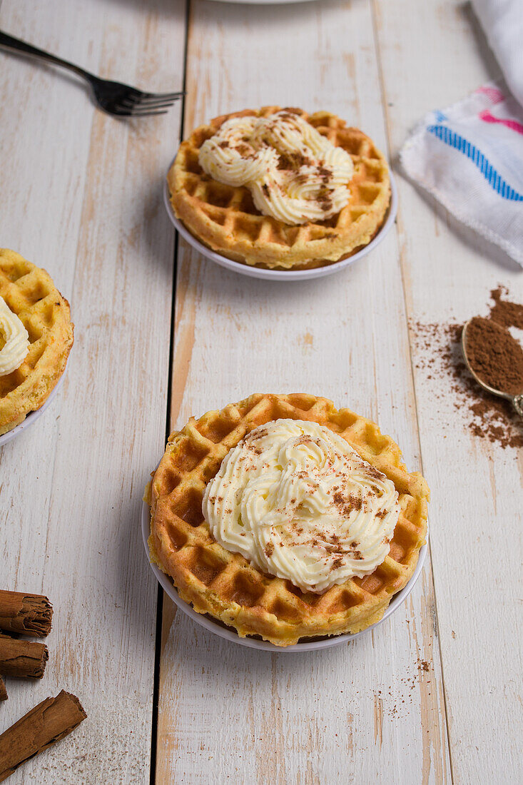 Von oben von frisch gebackenen hausgemachten Kürbis-Käse-Waffeln mit Zuckerguss auf Holztisch mit Zimtstangen in hellen Küche platziert