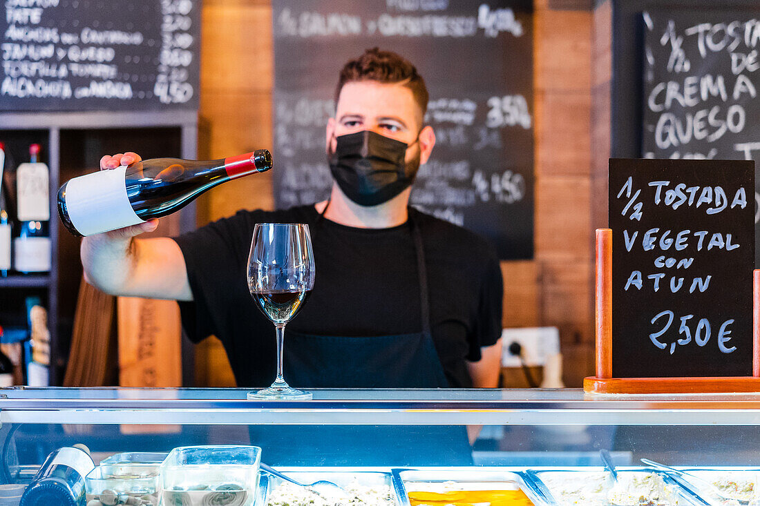 Anonymer Barkeeper gießt Wein aus einer Flasche in ein Glas am Tresen eines Restaurants mit vielen Schildern