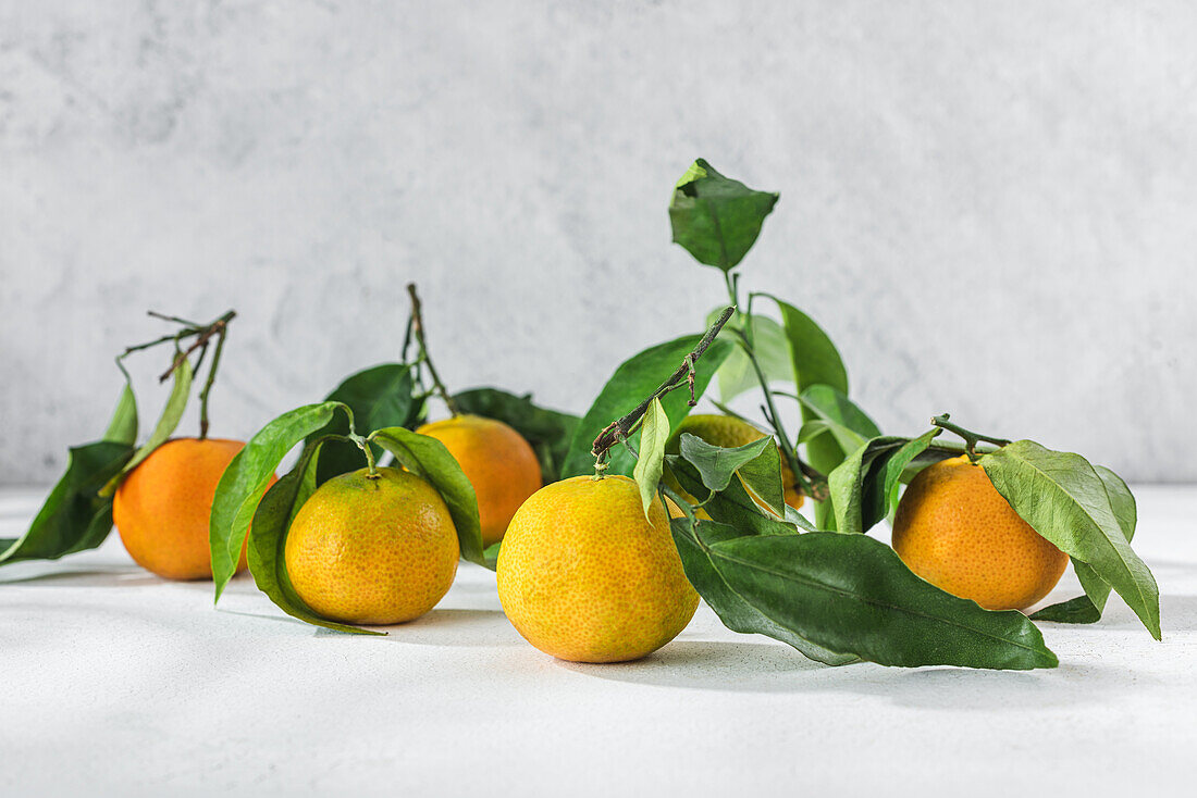 Orangefarbene Mandarinen mit grünem Stiel und Blatt liegen auf einem weißen Tisch