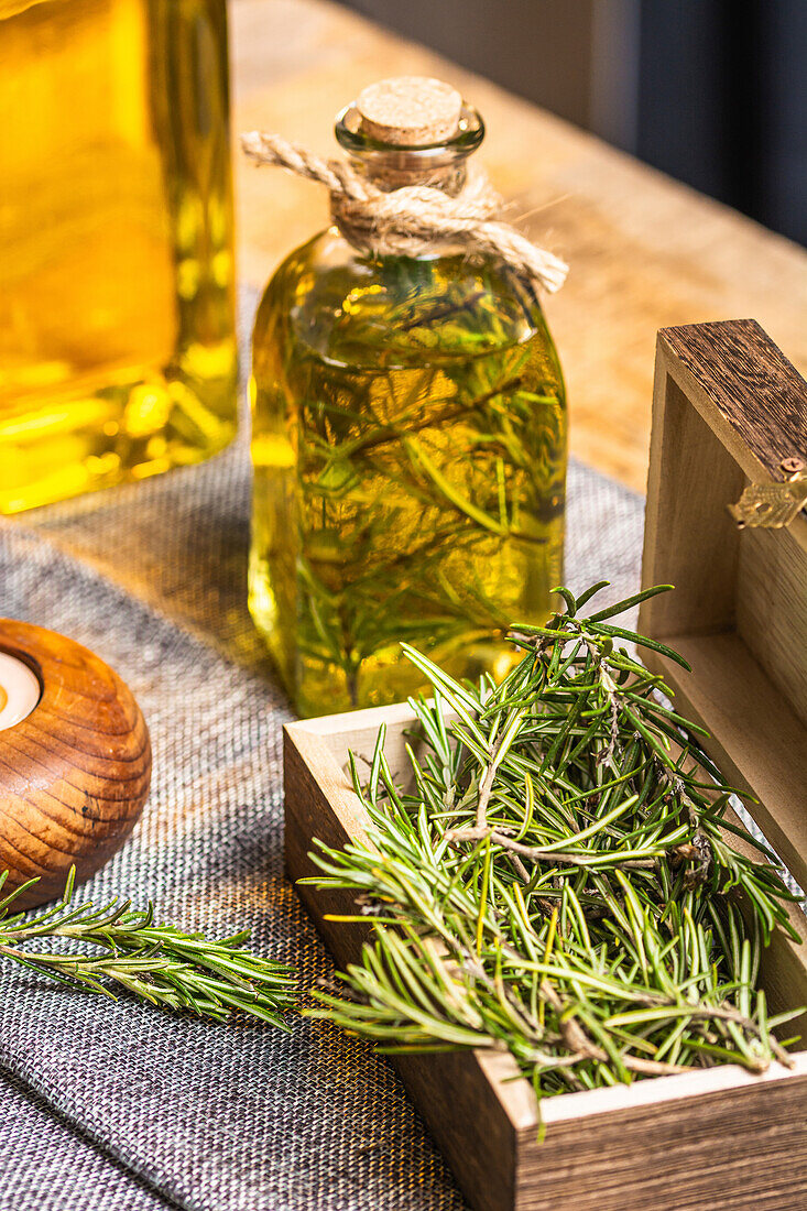 Glasflasche mit ätherischem Öl, Rosmarinzweigen und brennender Bio-Holzkerze auf grauem Tisch