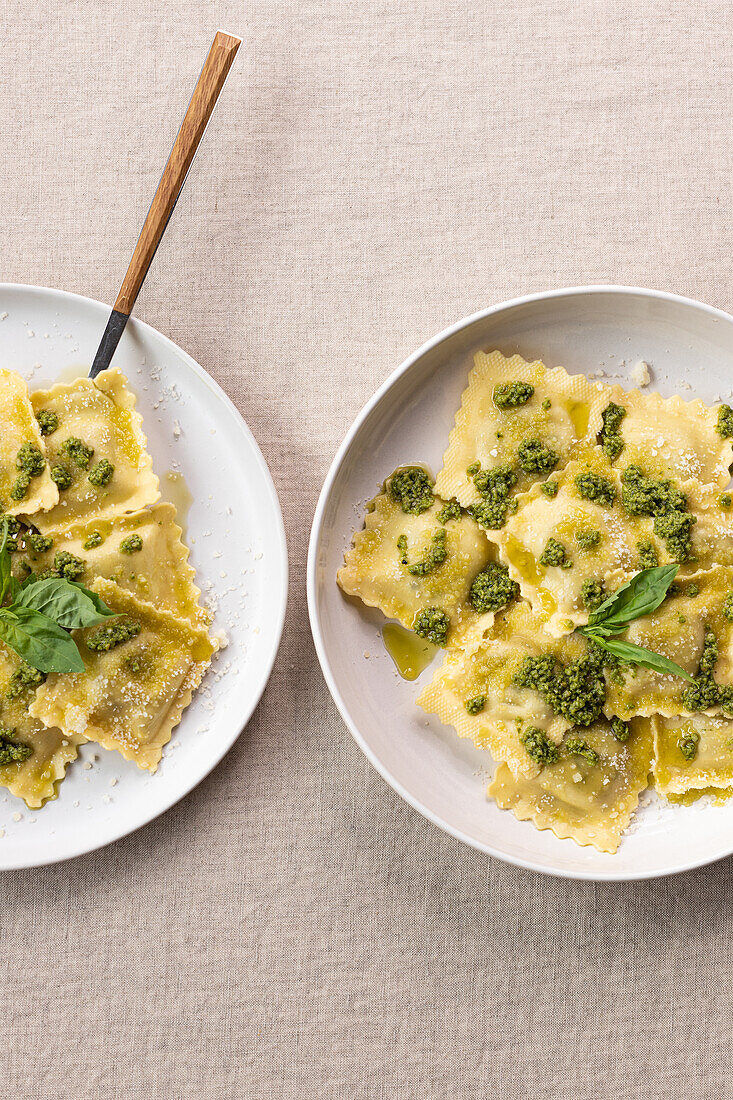 Von oben appetitlich gekochte Ravioli-Nudeln mit grüner Soße und Kräutern auf weißen Tellern mit Gabeln auf dem Tisch platziert