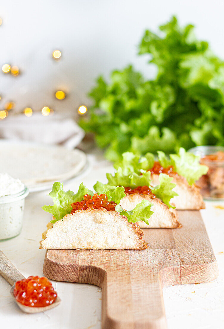 Kleine leckere Tacos mit rotem Kaviar und grünem Salat, serviert auf einem hölzernen Schneidebrett auf dem Tisch