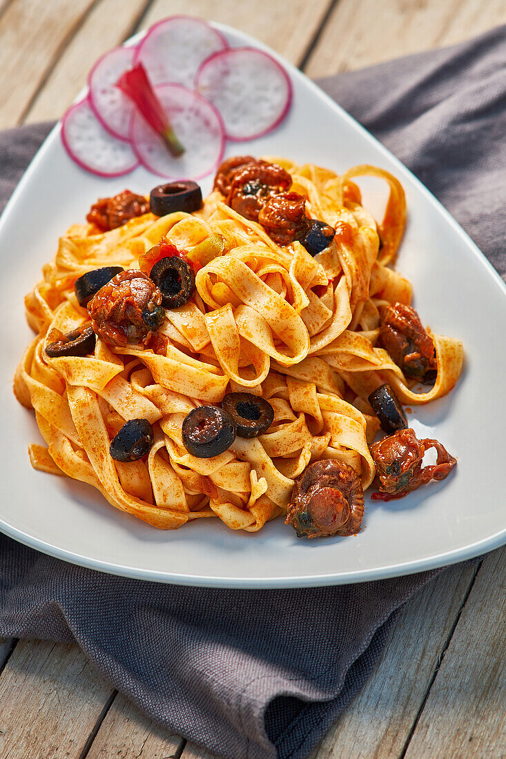 Eine köstliche Portion Fettuccine mit schwarzen Oliven, sonnengetrockneten Tomaten und einer reichhaltigen Tomatensauce, präsentiert auf einem weißen Teller