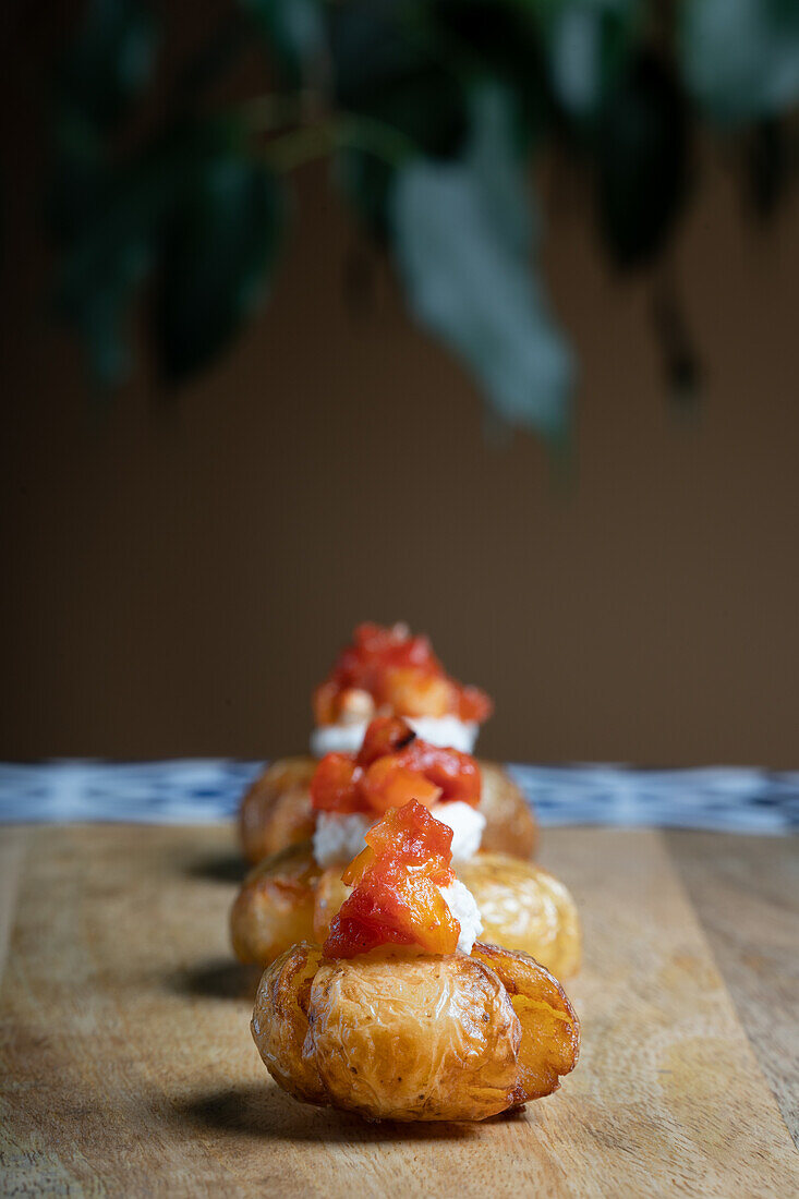 Köstliche Babykartoffel-Canapés, belegt mit cremigem Mozzarella-Käse und einer Garnierung aus gegrilltem rotem Pfeffer, präsentiert auf einem Holzbrett.