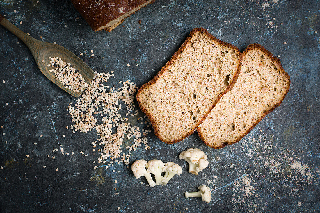 Draufsicht auf leckeres, frisch gebackenes Blumenkohlbrot auf einem Tisch mit Löffel in verstreutem Sesam in einer hellen Küche