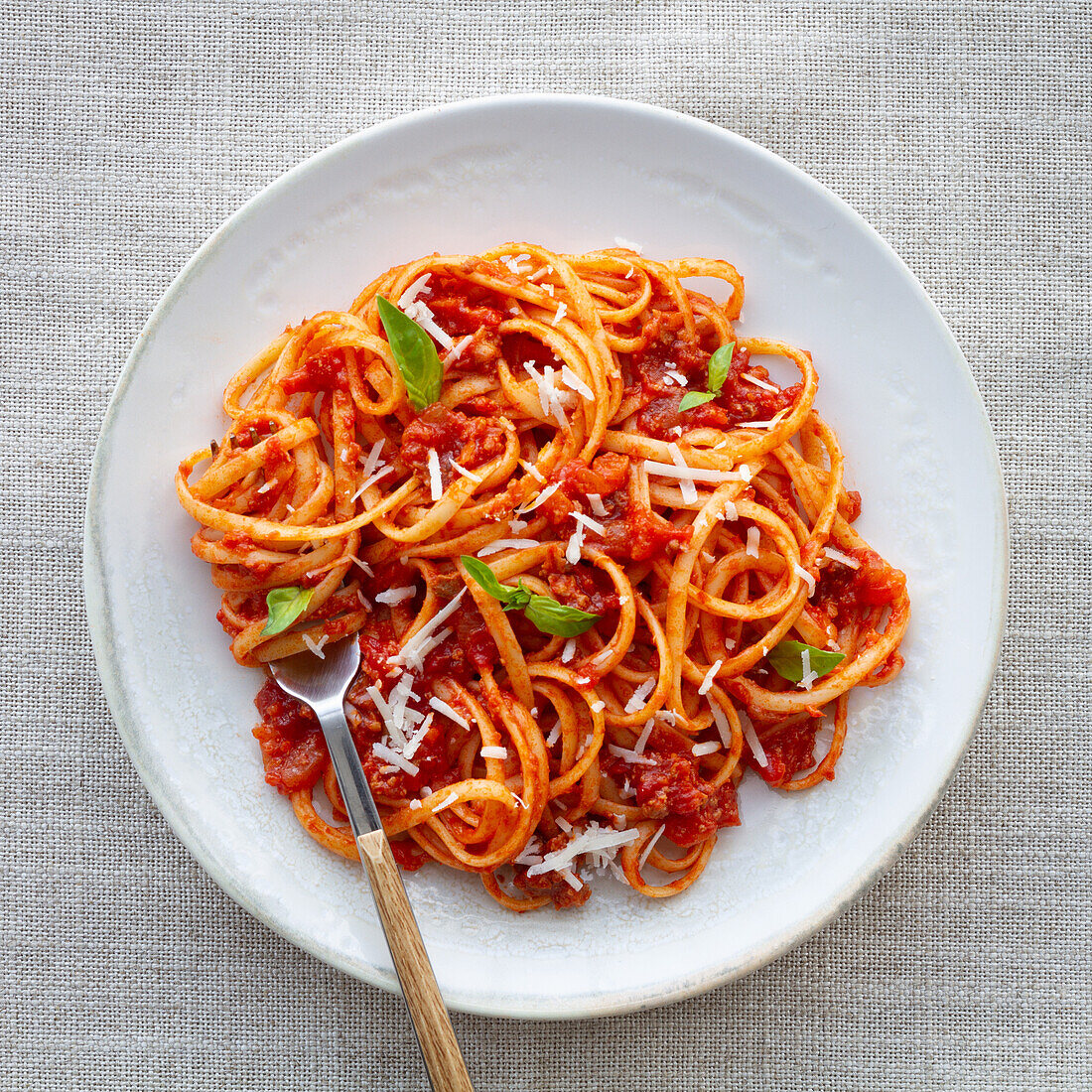 Blick von oben auf appetitliche hausgemachte Pasta mit Bolognesesoße, serviert mit frischen Basilikumblättern auf einem weißen Teller