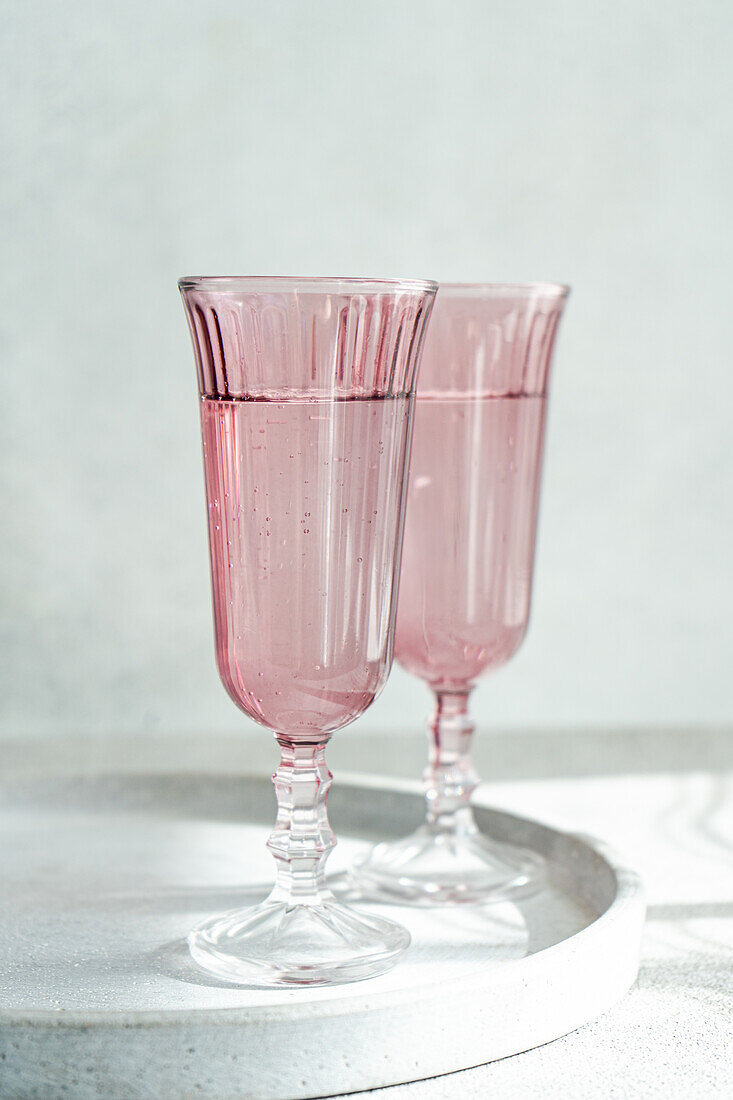 A duo of vintage-inspired pink glasses stands on a reflective surface, bathed in gentle sunlight with a minimalist background. Generative AI image