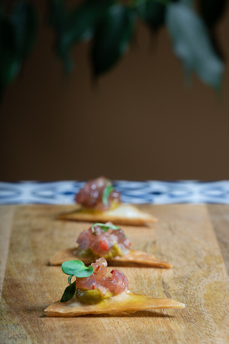 Delectable raw fresh salmon canapé with mustard on a crispy cracker garnished with fresh herbs, served on a wooden board.