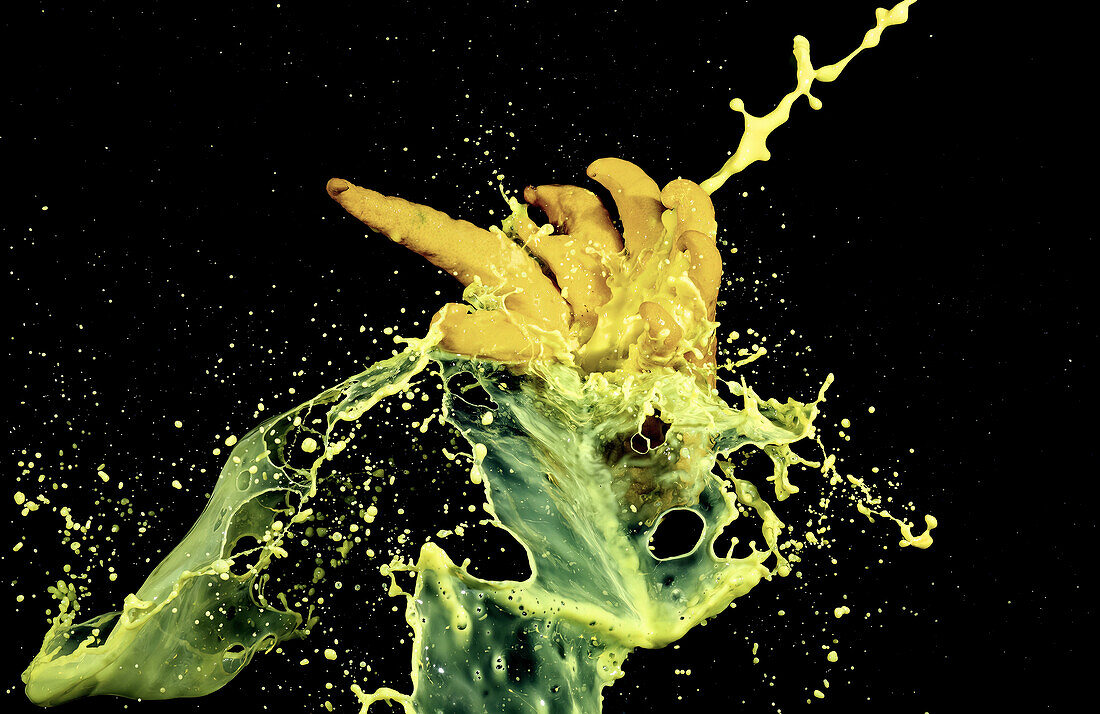 Dynamic splash of yellow and green paint captured in mid-air, resembling a Buddha's hand citron against a starry black background