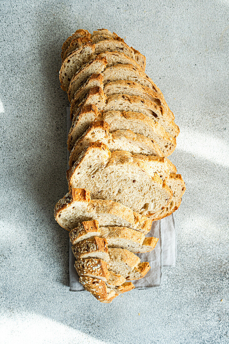 Draufsicht auf einen langen Laib Sauerteigbrot, der in Scheiben geschnitten und in einer Reihe auf einem Leinentuch mit grauem Hintergrund angeordnet ist