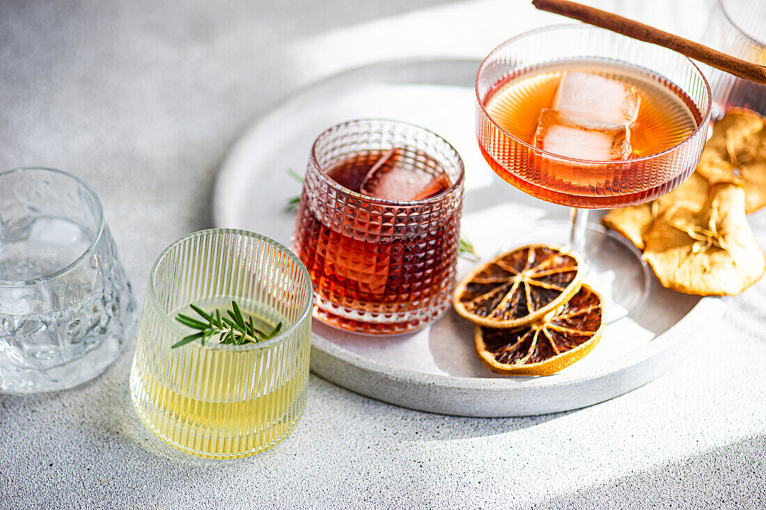 A diverse collection of spirits in ribbed glasses, including cherry liqueur with ice, limoncello with a rosemary sprig, and others, all resting tray with dried citrus decor