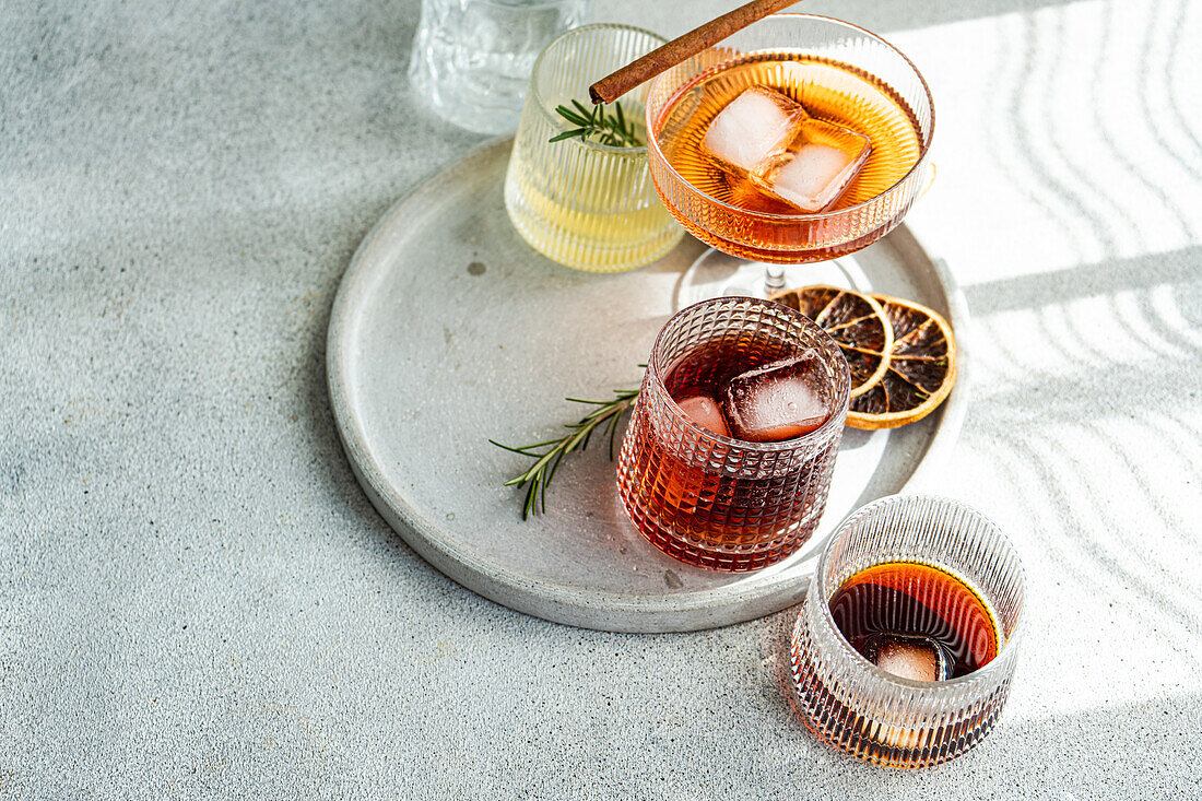 A diverse collection of fine spirits, served in textured glasses and garnished with botanicals and dried fruit, arranged on a round concrete tray