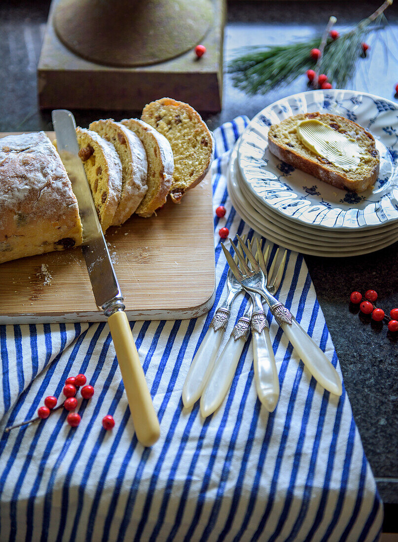 Geschnittener Stollen auf Holzbrett, Teller und Besteck auf gestreiftem Tuch