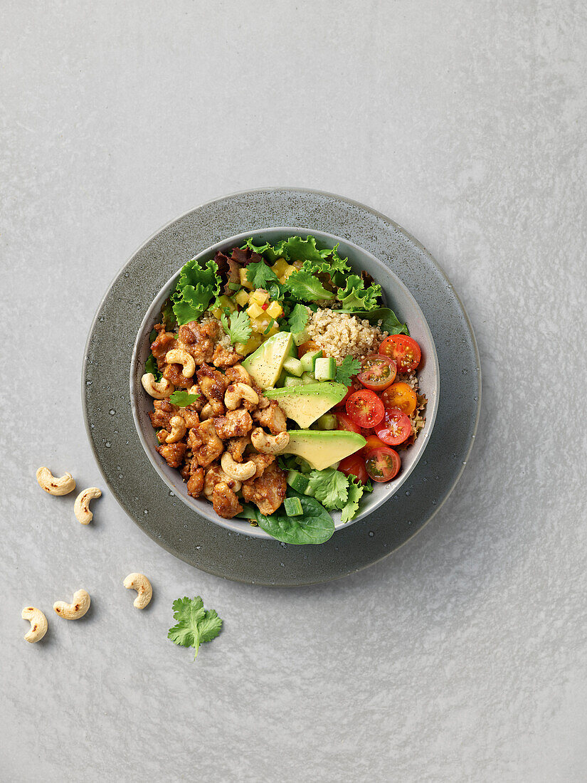 Quinoa bowl with tofu, avocado, cashew nuts and tomatoes