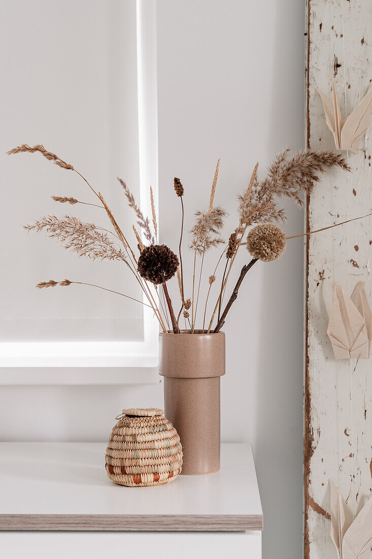 Dried flower arrangement and pompoms in a beige vase on a white table