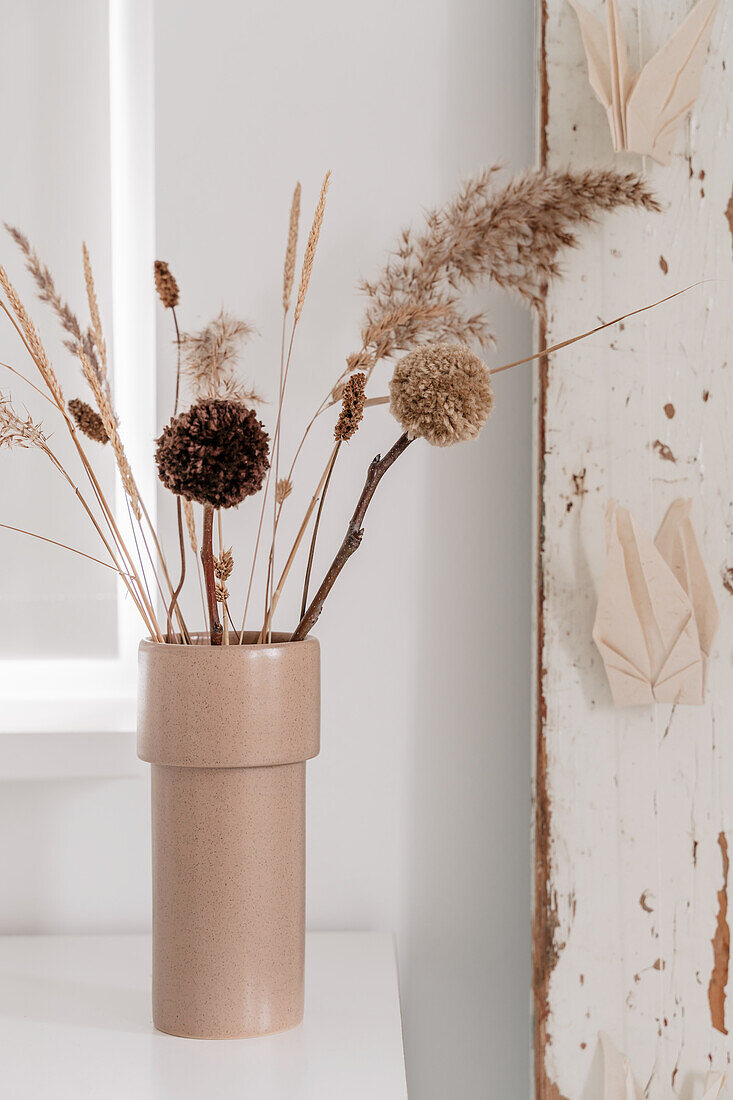 Trockenblumen und Pompons in beigefarbener Vase auf weißem Tisch