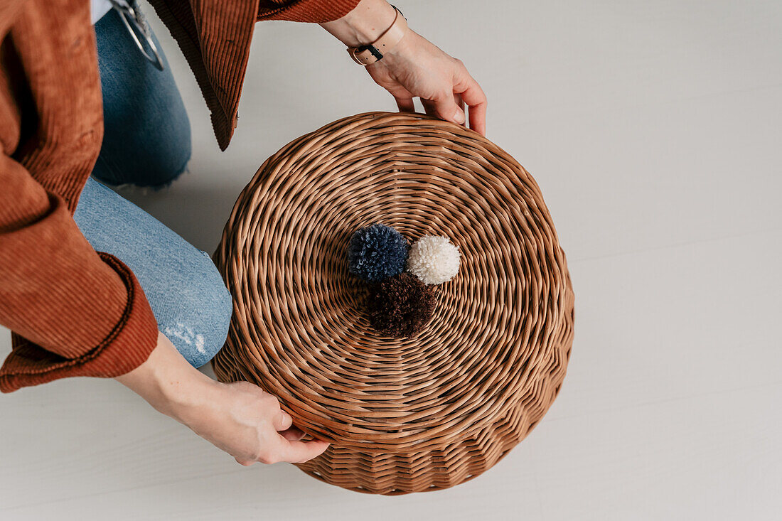 Geflochtener Korb mit drei Wollpompons in Blau, Weiß und Braun