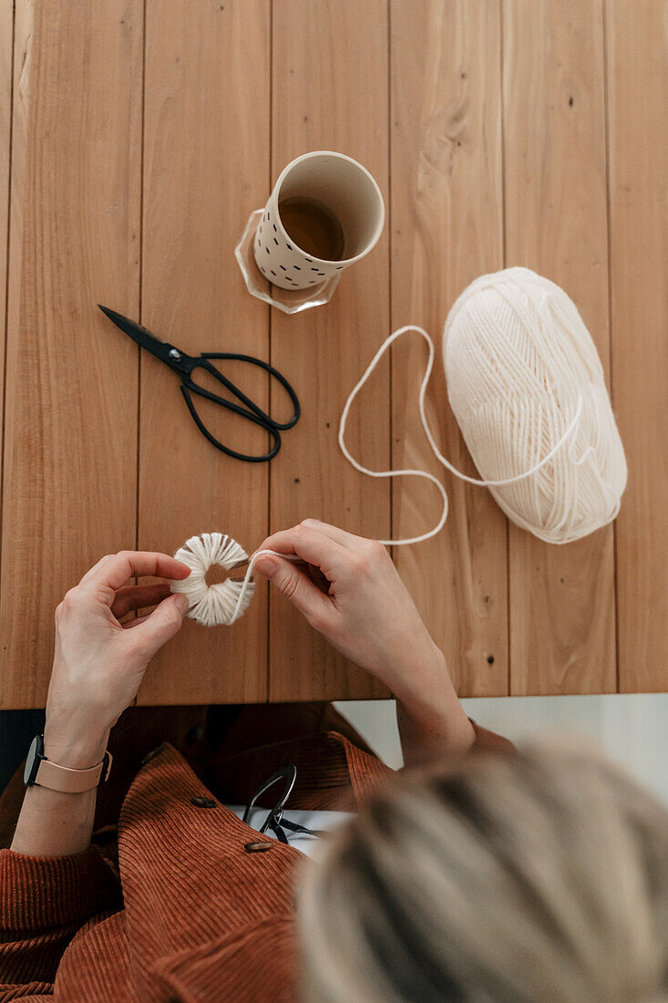 Hands crafting with wool and scissors on a wooden table