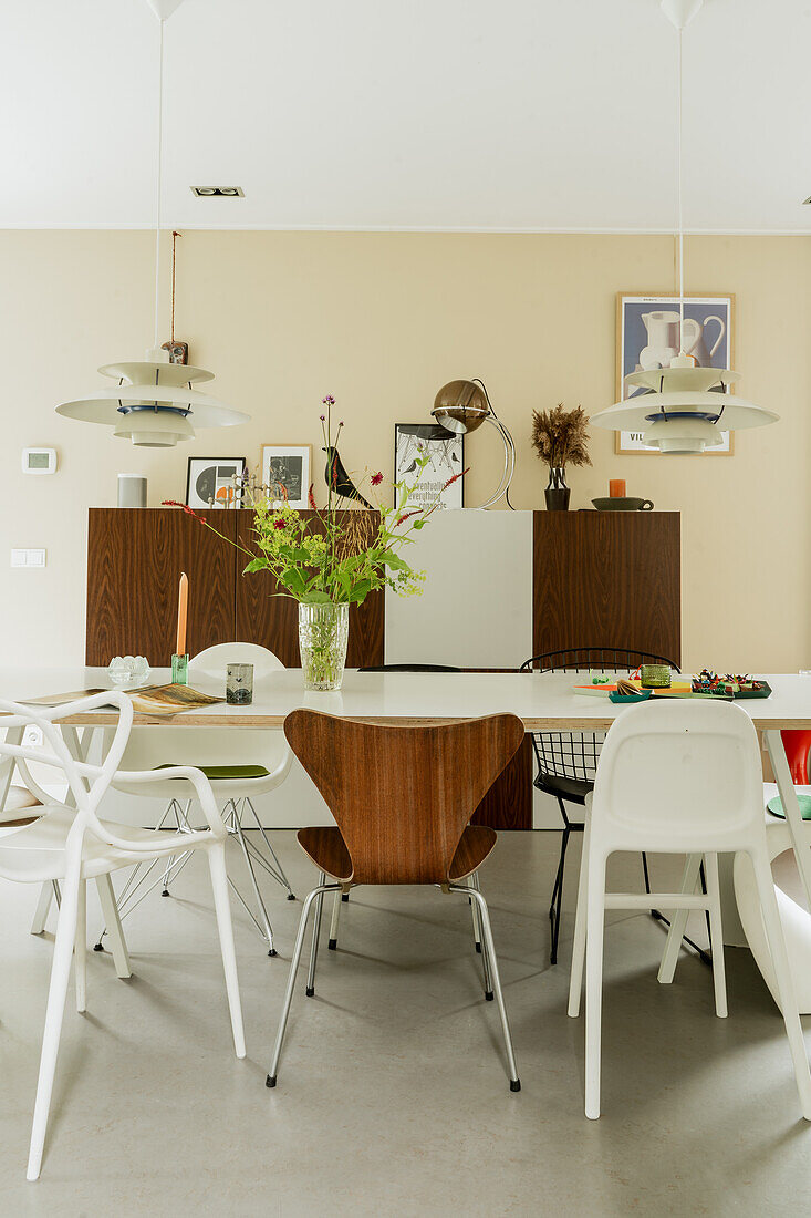 Modern dining area with various chairs and a bouquet of flowers on a white table