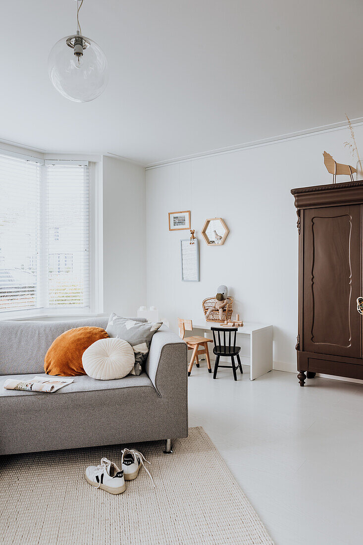 Lichtdurchflutetes Wohnzimmer mit grauem Sofa und Vintage-Schrank