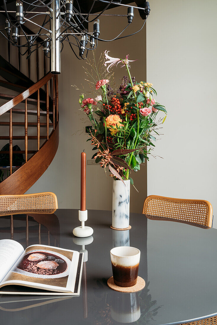 Runder Esstisch mit Blumenstrauß in Marmorvase, Buch und Kerze unter moderner Hängelampe