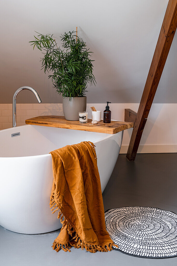 Freestanding bathtub with wooden shelf and plant, towel and carpet