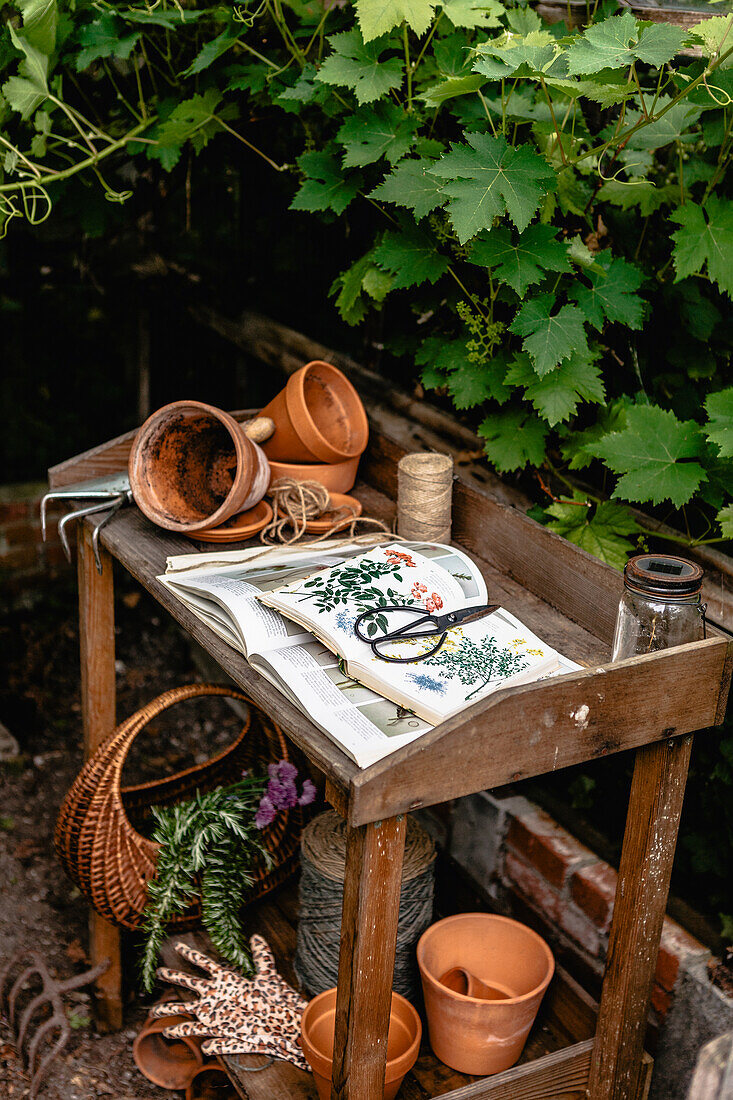 Pflanztisch im Garten mit Tontöpfen, Büchern und Schere