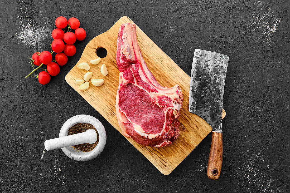 Ribeye steak with bone on cutting board, garlic and cleaver