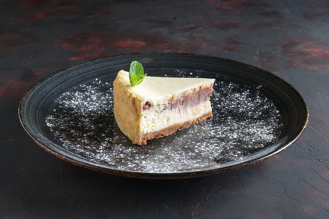 Cheesecake slice with mint leaf on a black plate