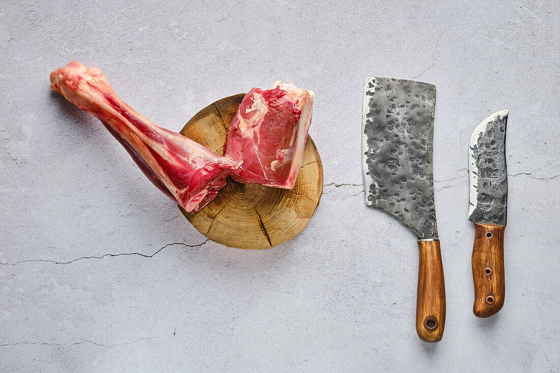 Raw venison leg on a chopping block with butcher's cleavers