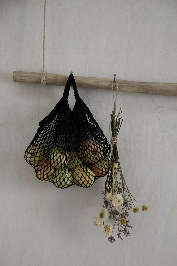 Apples hung in a net next to dried flowers