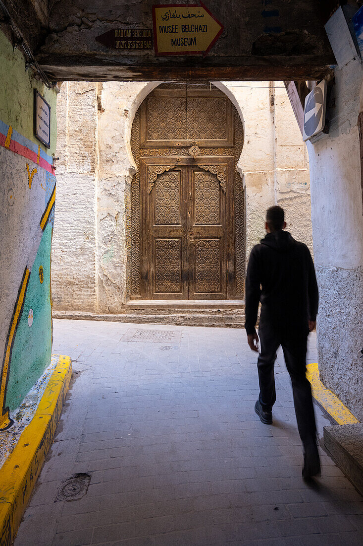 Ein junger Mann geht durch eine enge Gasse in den labyrinthartigen Straßen der Medina von Fez, Marokko.