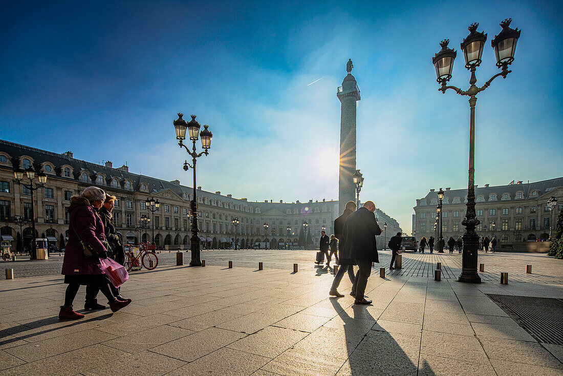 Silhouetten von Fußgängern, die in der Wärme der untergehenden Sonne am Place Vendome in Paris spazieren gehen.