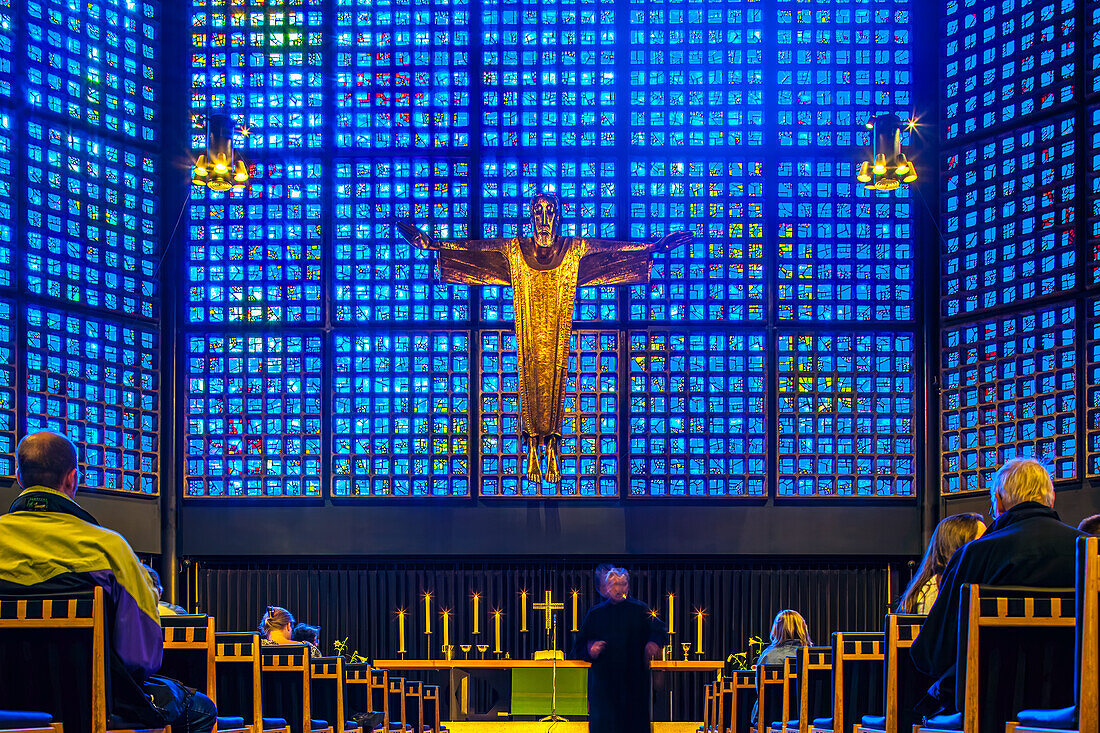 Congregants sit in peaceful reflection before the illuminated crucifix at Kaiser Wilhelm Memorial Church, Berlin, Germany