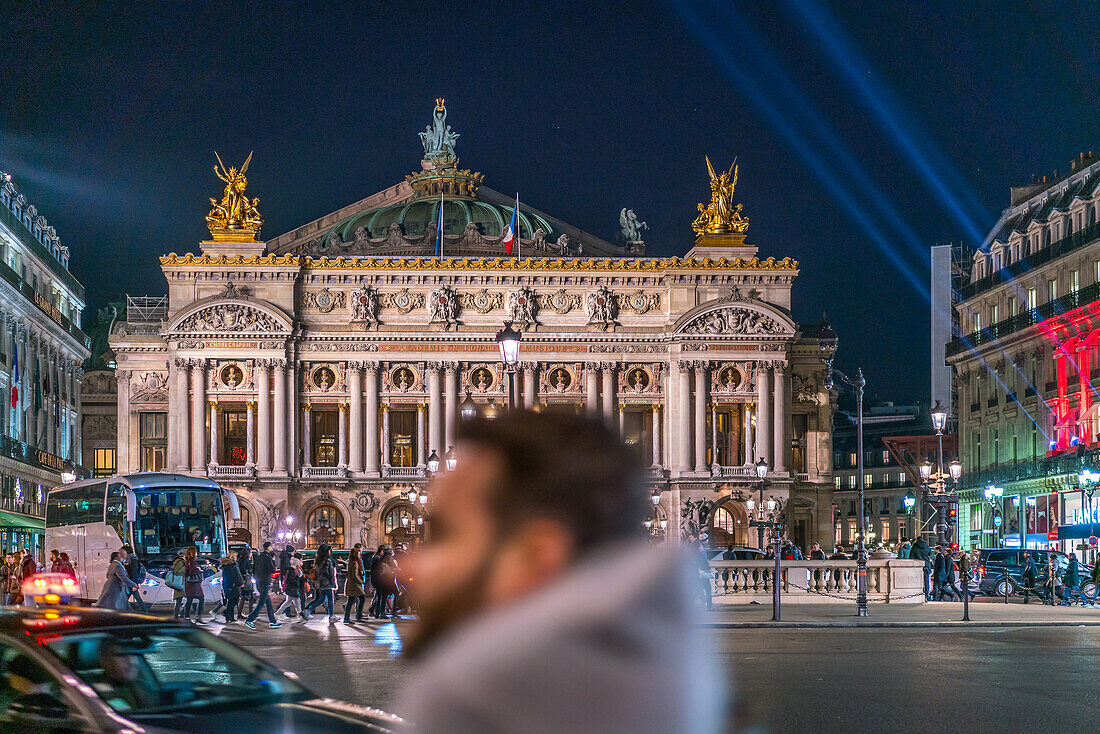 Palais Garnier Opera House illuminated at dusk with city life bustling in foreground.