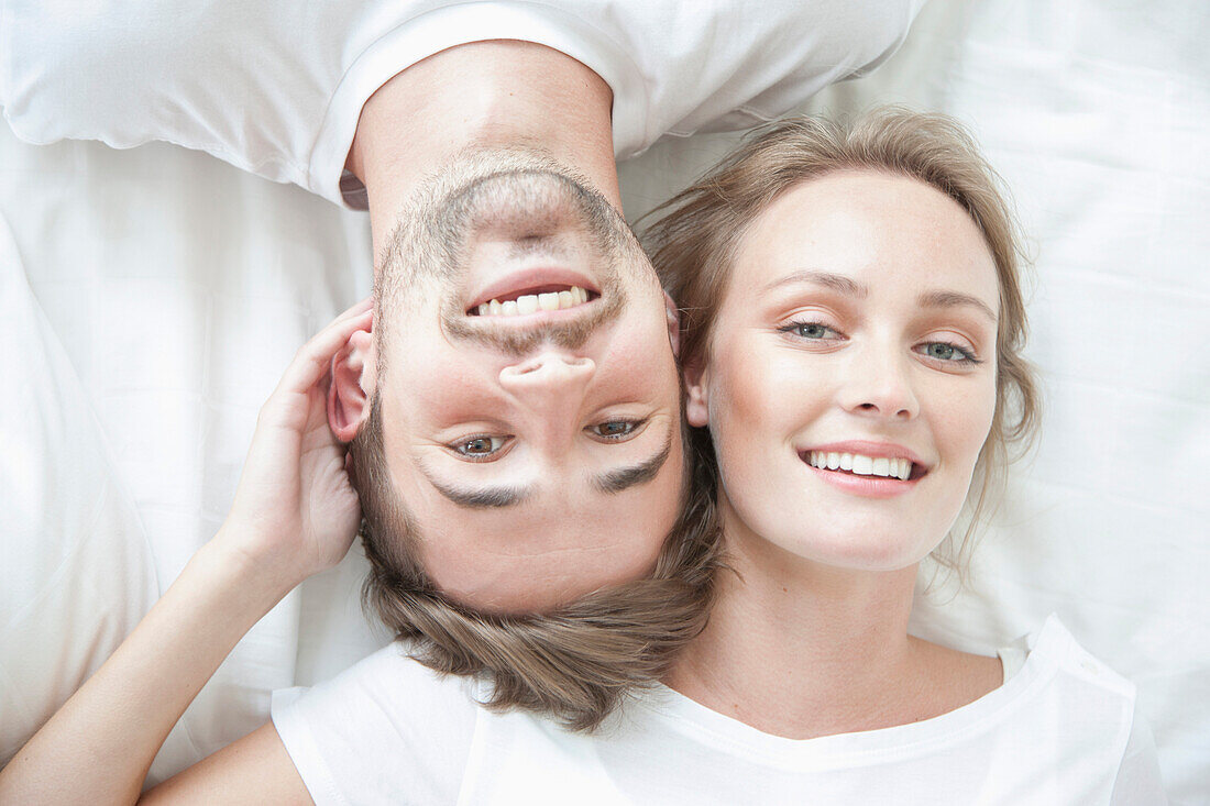 Smiling Couple Lying on Bed Facing Opposite Directions