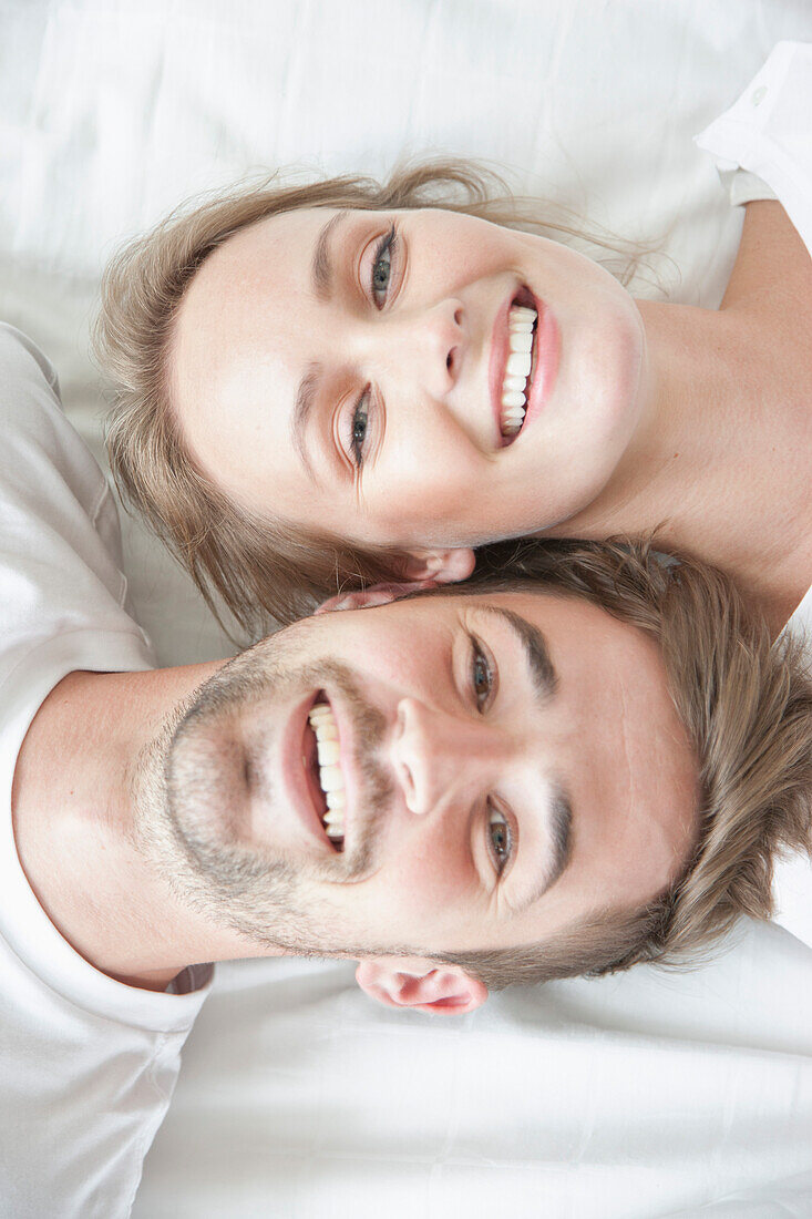 Smiling Couple Lying on Bed Facing Opposite Directions