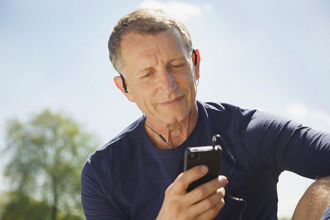 Nahaufnahme eines reifen Mannes im Park, der mit seinem Smartphone Musik hört