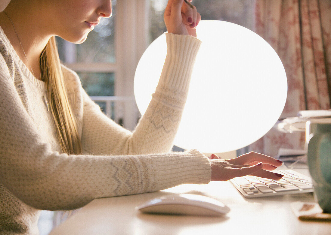 Profil einer Frau, die vor einer Kugellampe auf einer Computertastatur tippt, Nahaufnahme