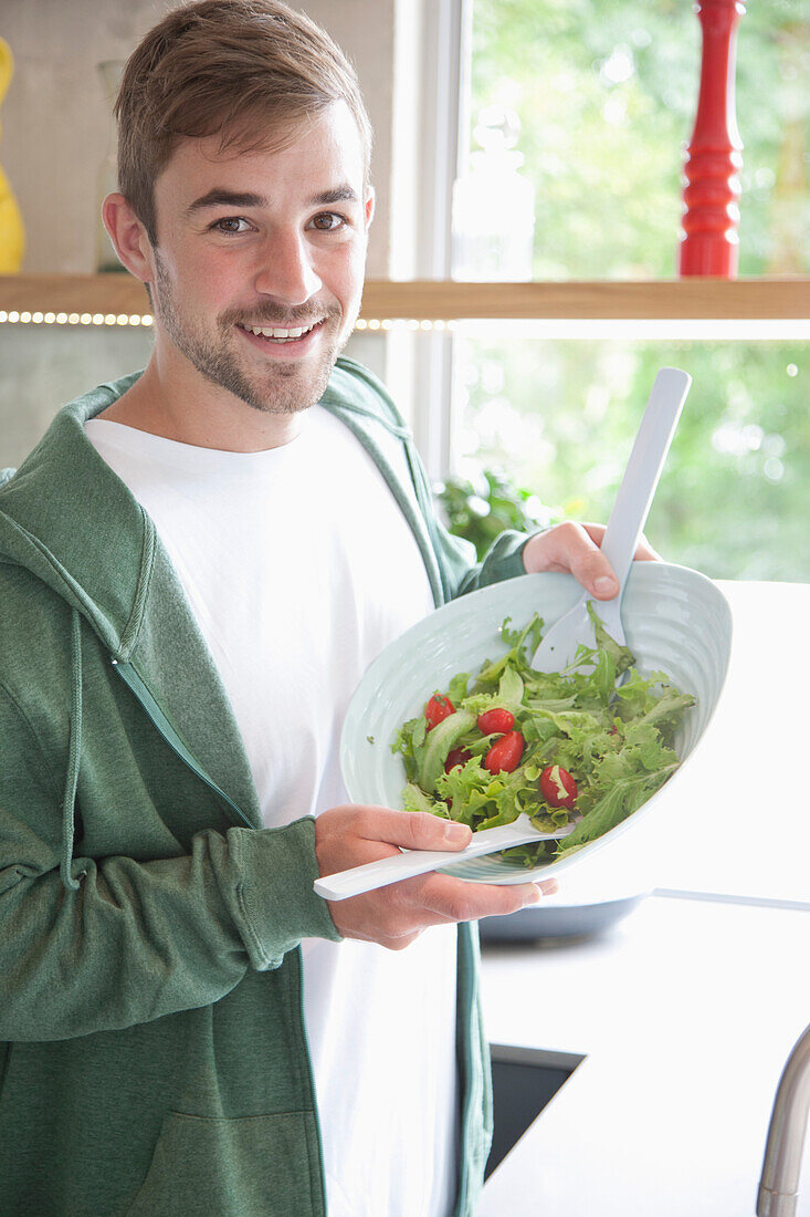 Mann hält lächelnd eine Schüssel mit Salat