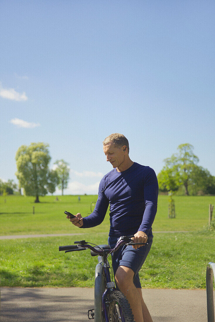 Älterer Mann im Park mit Fahrrad, der mit seinem Smartphone Musik hört